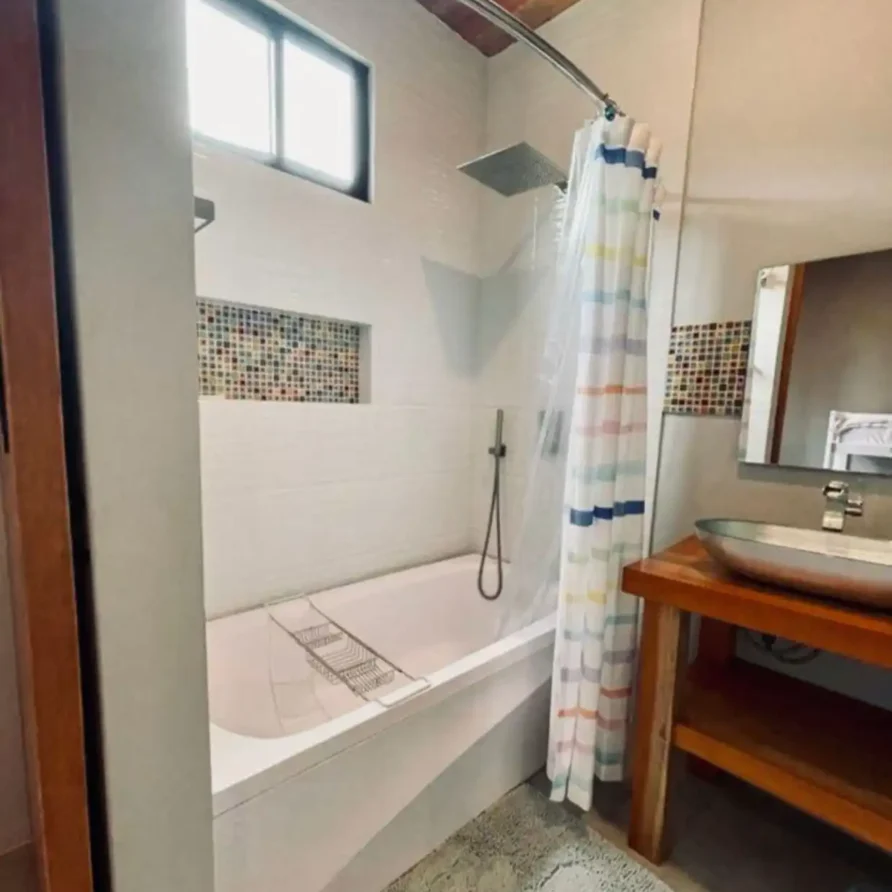 Moderno baño con bañera y ducha, cortina de colores, lavabo ovalado y techo de madera en Casa Kommo12.