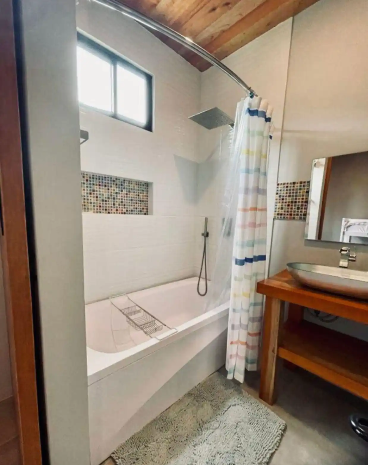 Moderno baño con bañera y ducha, cortina de colores, lavabo ovalado y techo de madera en Casa Kommo12.