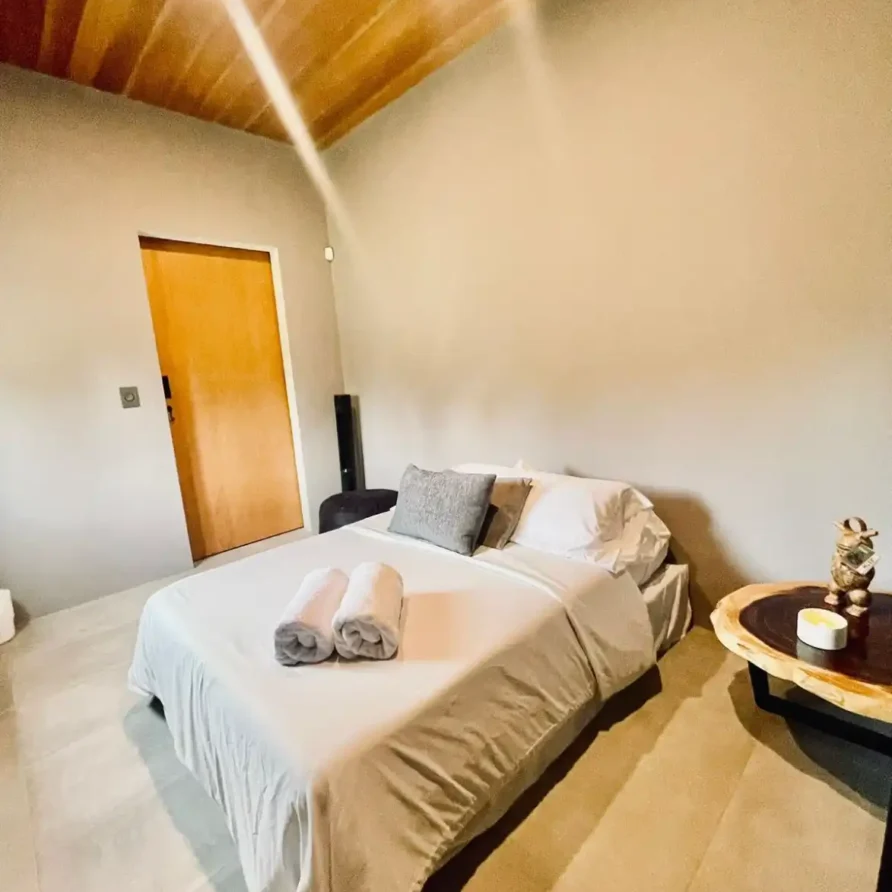 Dormitorio moderno en casa campestre con techo de madera y cama blanca, ideal para descanso cerca de Lago Calima.