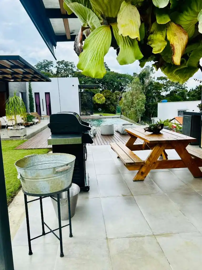 Patio moderno de casa campestre con piscina, parrilla BBQ y mesa de pícnic. Ideal para relax y reuniones.