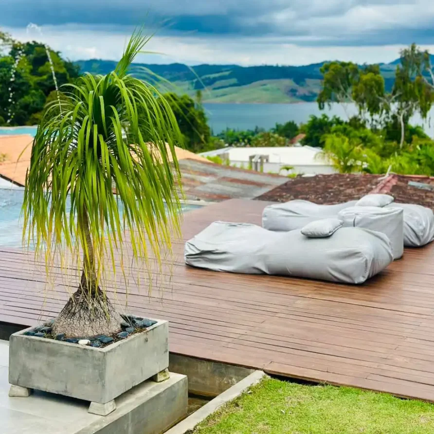 Terraza de madera con planta tropical y tumbonas grises, ofreciendo vista al Lago Calima y montañas desde una casa campestre.