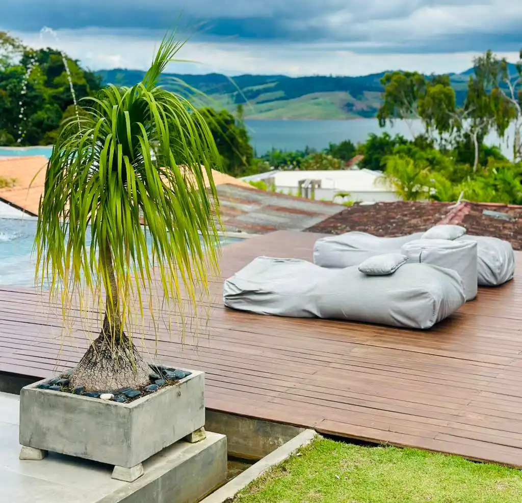 Terraza de madera con planta tropical y tumbonas grises, ofreciendo vista al Lago Calima y montañas desde una casa campestre.