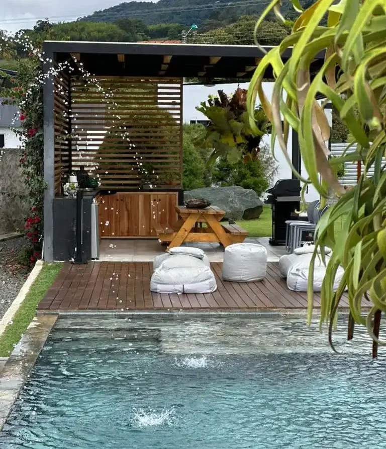 Piscina y zona social de casa campestre en Lago Calima con pérgola, deck de madera y pufs, rodeada de naturaleza.