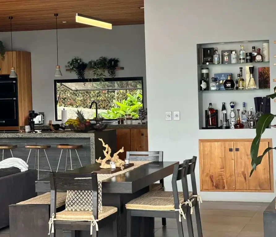 Interior de hermosa casa campestre moderna con cocina, comedor y barra de bar, rodeada de exuberante vegetación.