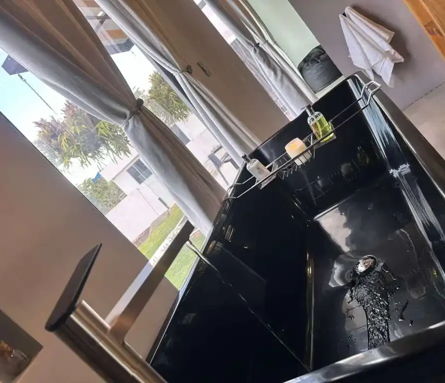 Bañera negra moderna con grifo elegante y vista a un paisaje verde, en una hermosa casa campestre.