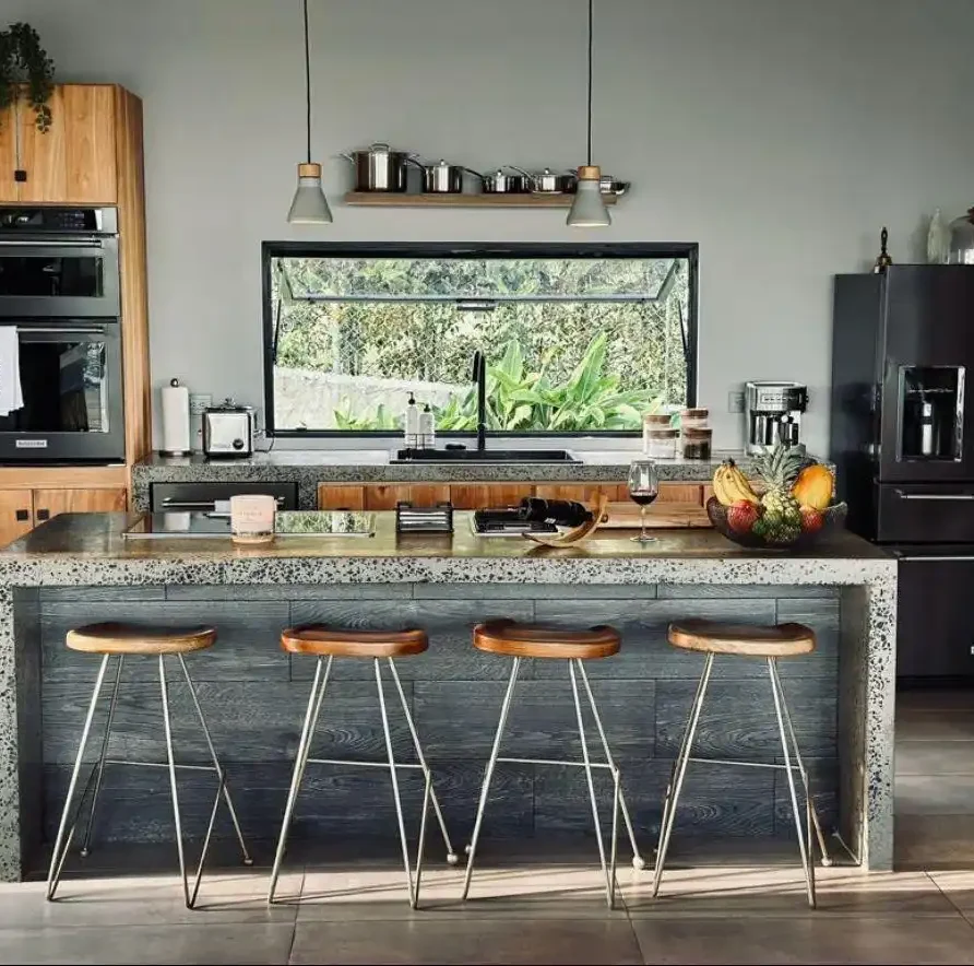 Cocina moderna en casa campestre con isla central, taburetes de madera y ventanal con vista al jardín.