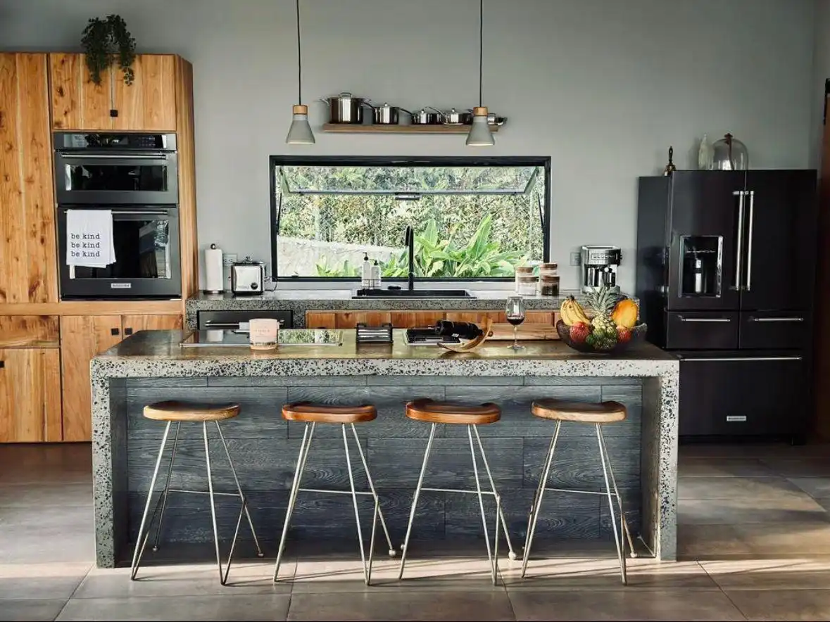 Cocina moderna en casa campestre con isla central, taburetes de madera y ventanal con vista al jardín.