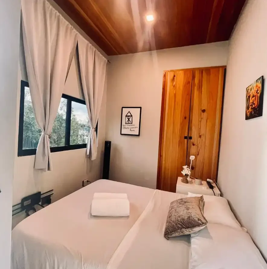 Dormitorio moderno en Casa Kommo con cama blanca, techo de madera y armario rústico, ideal para Casa campestre Lago Calima.