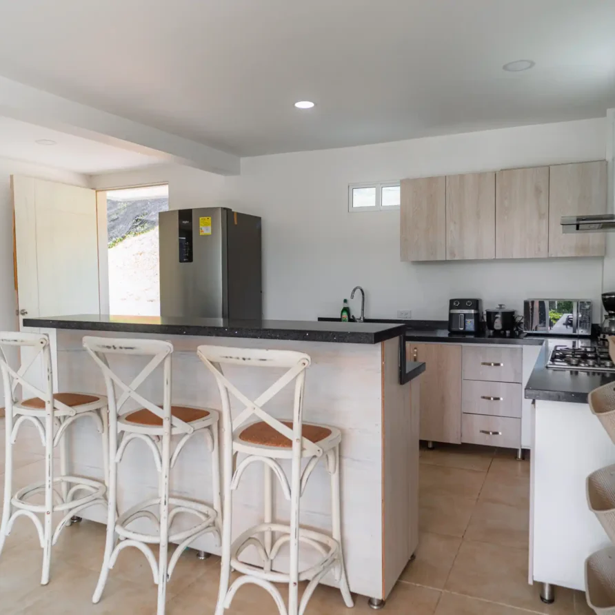 Cocina moderna y equipada con barra, sillas altas y electrodomésticos de acero en cabaña del Lago Calima.