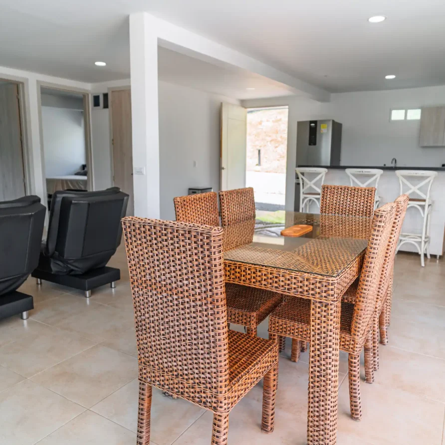Interior moderno de cabaña Casa Curva Bonita con comedor de mimbre, recliners negros y cocina integrada.
