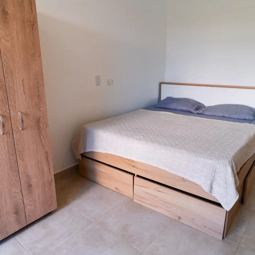 Dormitorio luminoso con cama de madera clara, base de almacenamiento y armario a juego. Ideal para casas de alquiler.