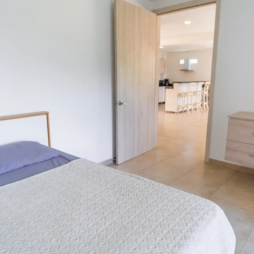 Dormitorio moderno en Casa Curva Bonita, con cama y acceso directo a cocina, ideal para cabaña Lago Calima.