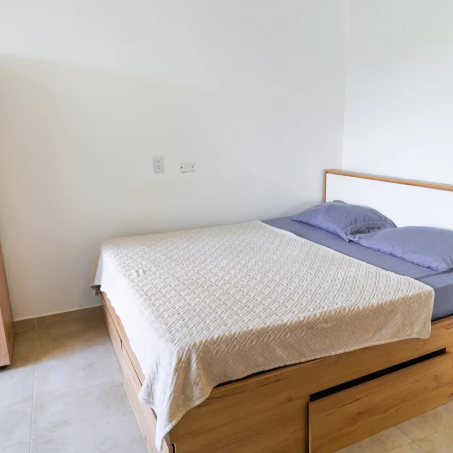 Dormitorio moderno con cama de madera, cabecero blanco, y armario, ideal para una estancia en Casa Curva Bonita, Lago Calima.