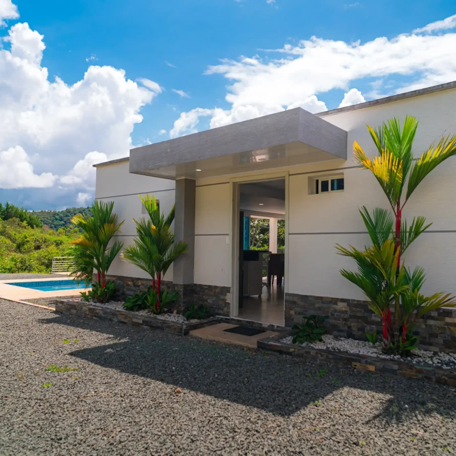 Exterior de moderna casa blanca con piscina, palmeras y entrada, frente a paisaje verde cerca del Lago Calima.