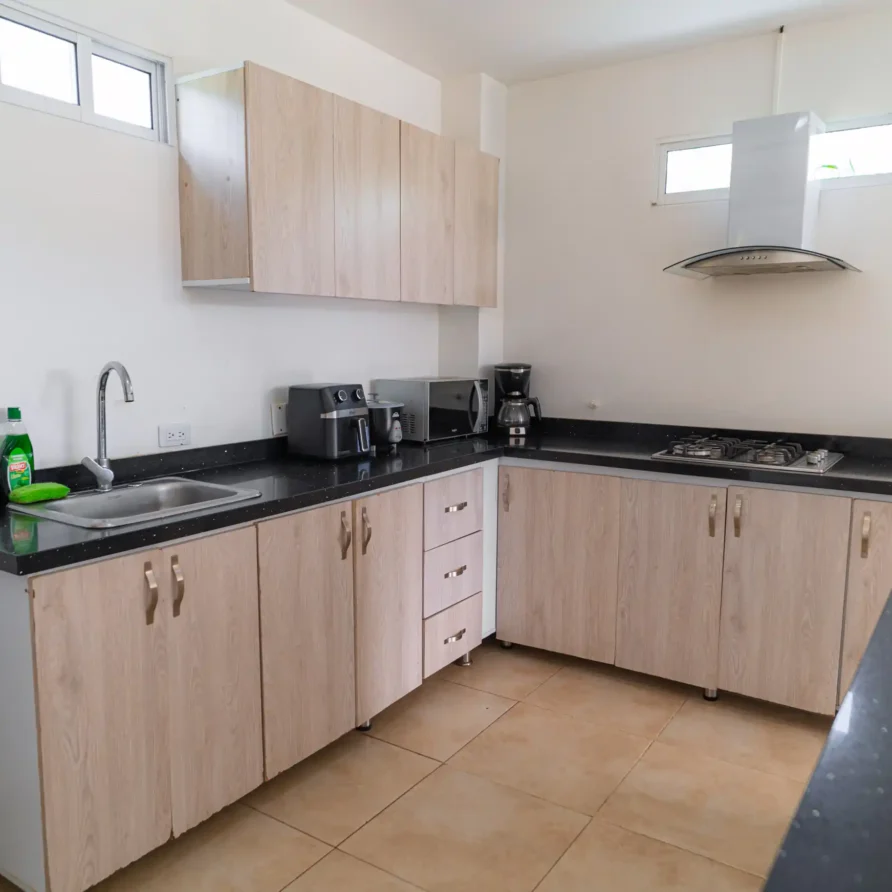 Cocina moderna equipada en cabaña cerca del Lago Calima, con gabinetes de madera clara y encimeras negras.