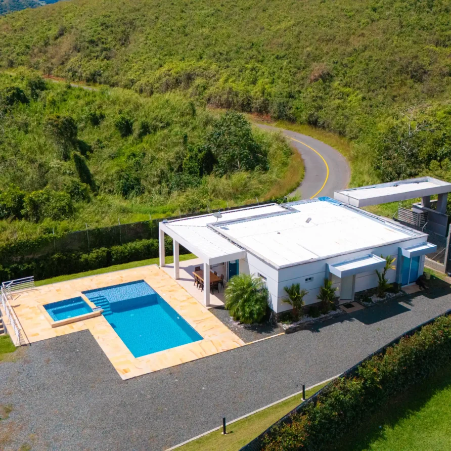 Moderna casa blanca con piscina azul y jacuzzi, rodeada de verdes colinas y carretera sinuosa cerca de Lago Calima.