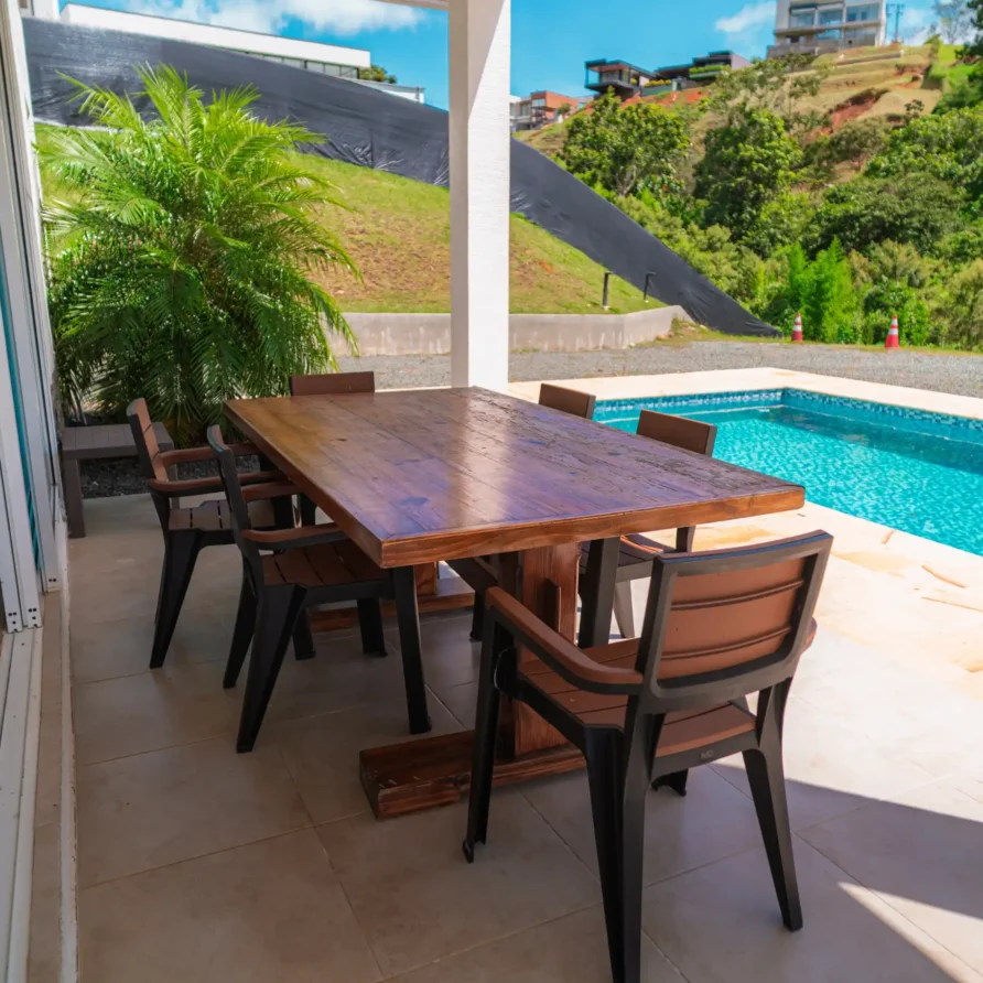Terraza exterior de cabaña con mesa de madera, sillas y piscina, en un entorno verde cerca del Lago Calima.