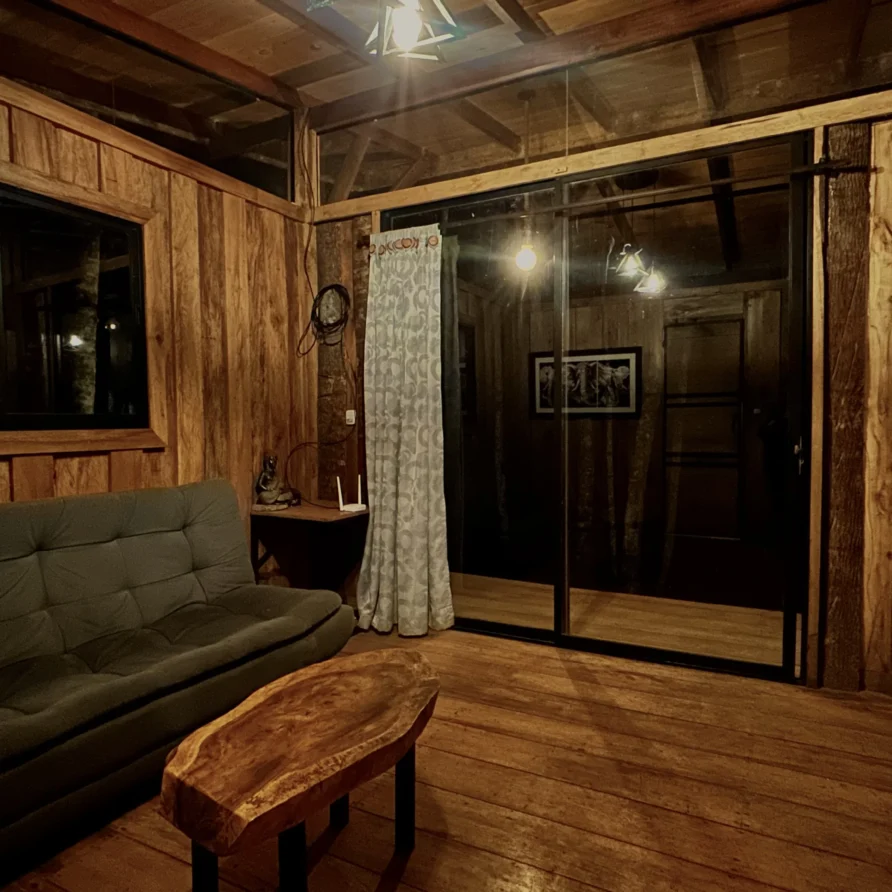 Planes Turisticos 110 Interior de cabaña Crisálida: sala acogedora, cocina compacta y ambiente cálido de madera, perfecta para dos.