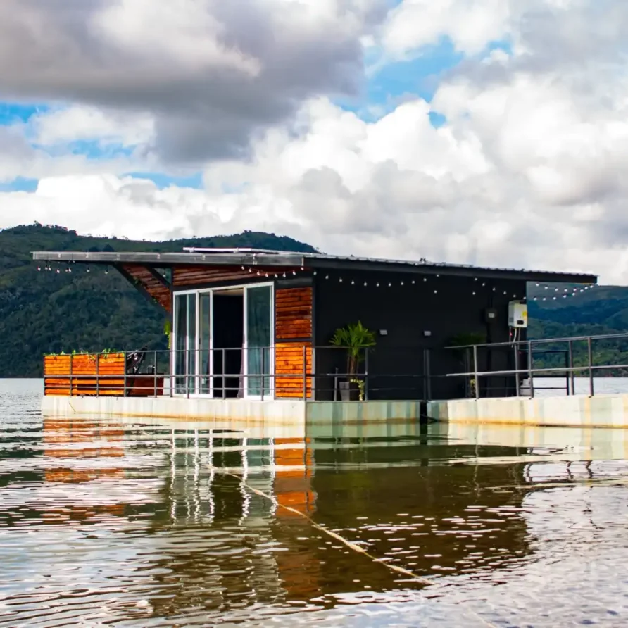 Cabaña flotante moderna en el Lago Calima, rodeada de glamping de tiendas y paisaje montañoso colombiano.