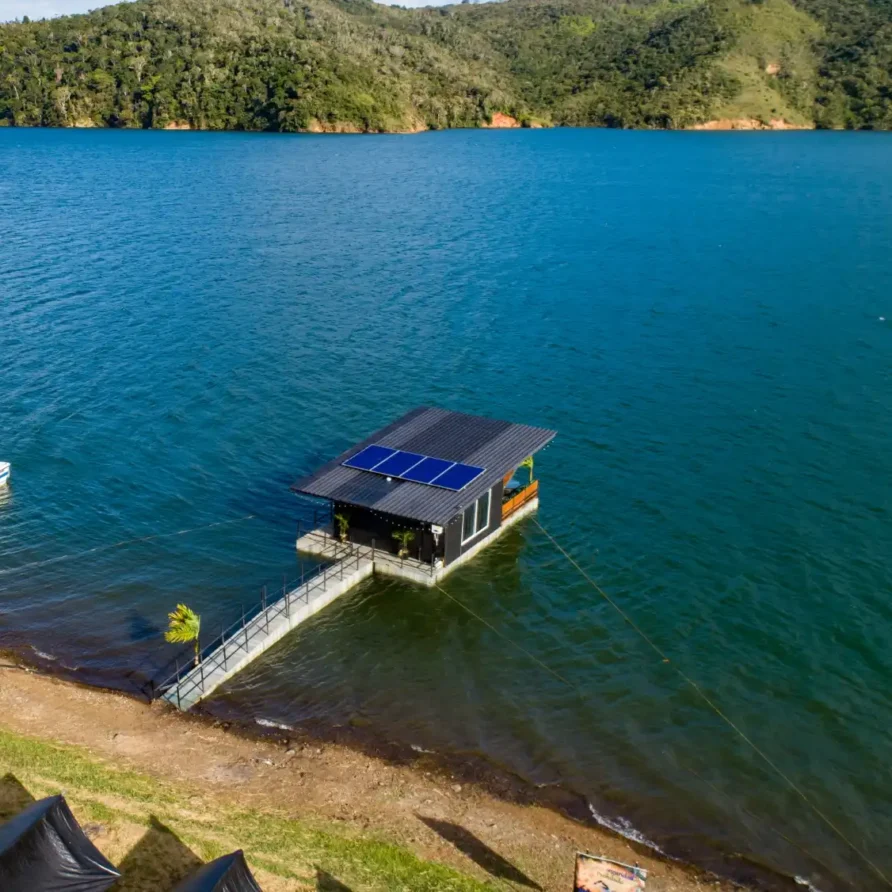 Glamping flotante moderno con paneles solares en el Lago Calima, Colombia, conectado por muelle a la orilla.
